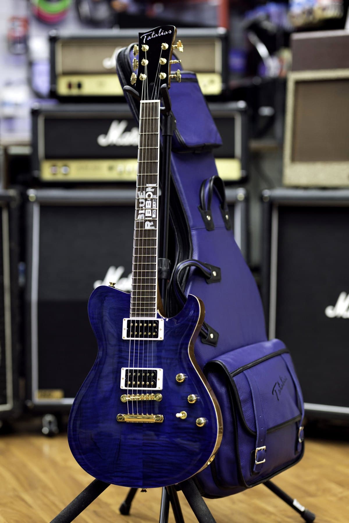 A handmade Tatalias figured-top in blue with its custom gig bag in front of the amp wall